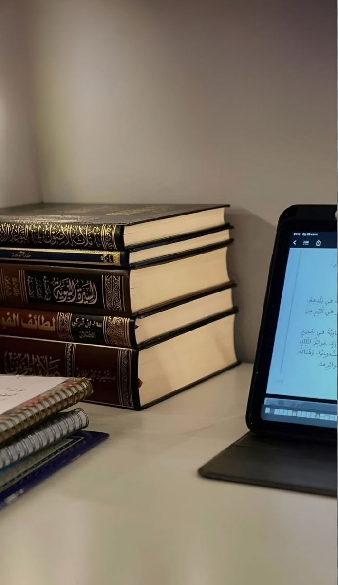 كتب العلوم الشرعية بجوار جهاز لوحي يعرض نصاً قرآنياً